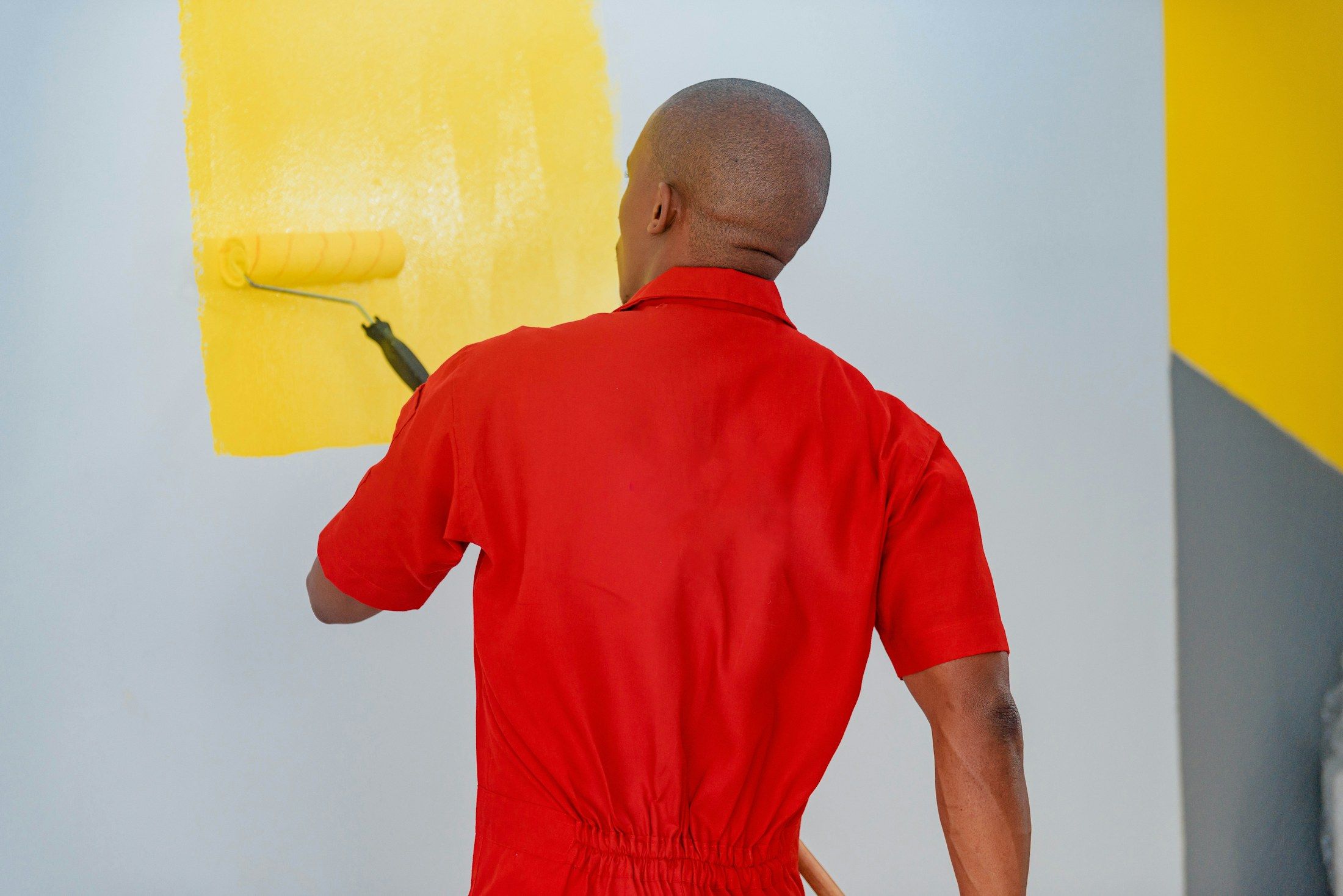 Pintor a aplicar tinta amarela numa parede com rolo